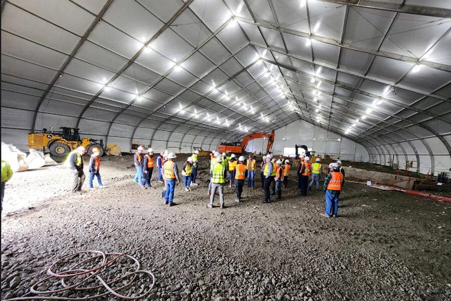 workers standing under large construction tent with interior lighting